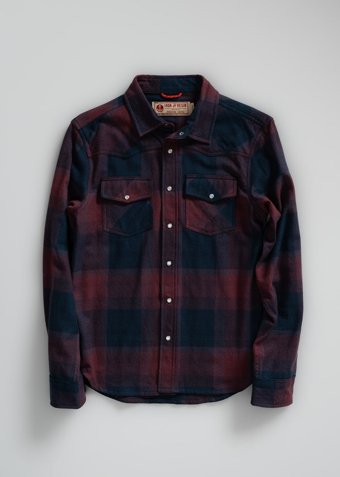 A red and navy plaid flannel shirt with snap buttons and chest pockets, laid flat on a light background.