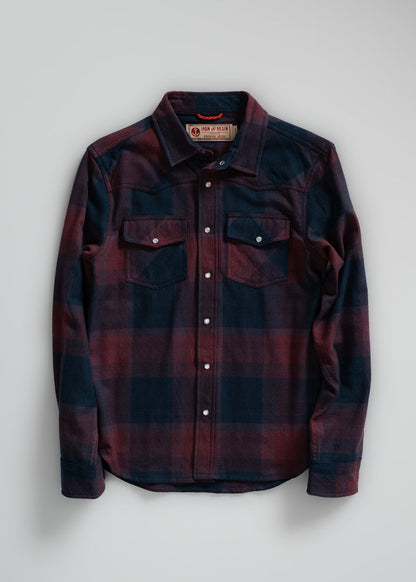 A red and navy plaid flannel shirt with snap buttons and chest pockets, laid flat on a light background.