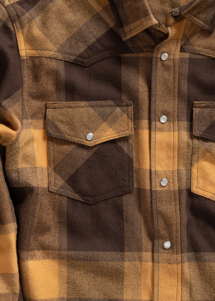 Close-up of a brown and yellow plaid flannel shirt with snap buttons and two chest pockets, showcasing its textured fabric.