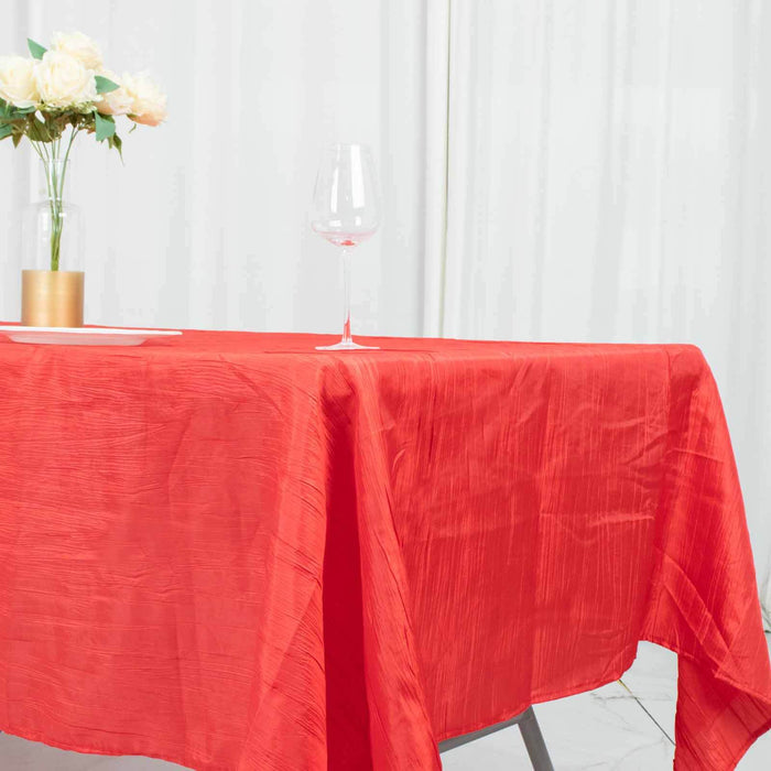Red tablecloth draped over a table with a glass and flowers in the background.