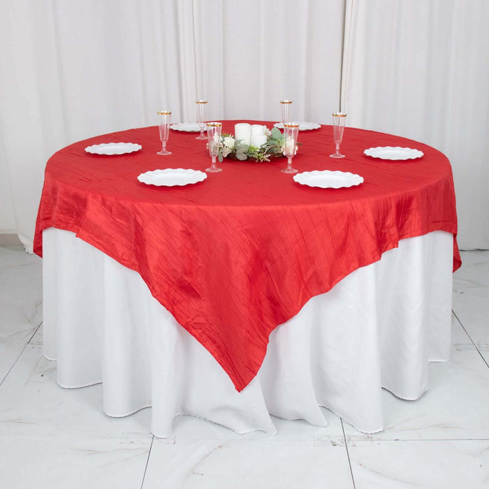 Red tablecloth draped elegantly over a round table with white plates and candles.