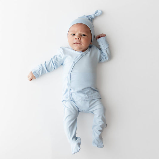 Newborn laying on a light neutral surface wearing the Take Me Home Set with Cap in Breeze