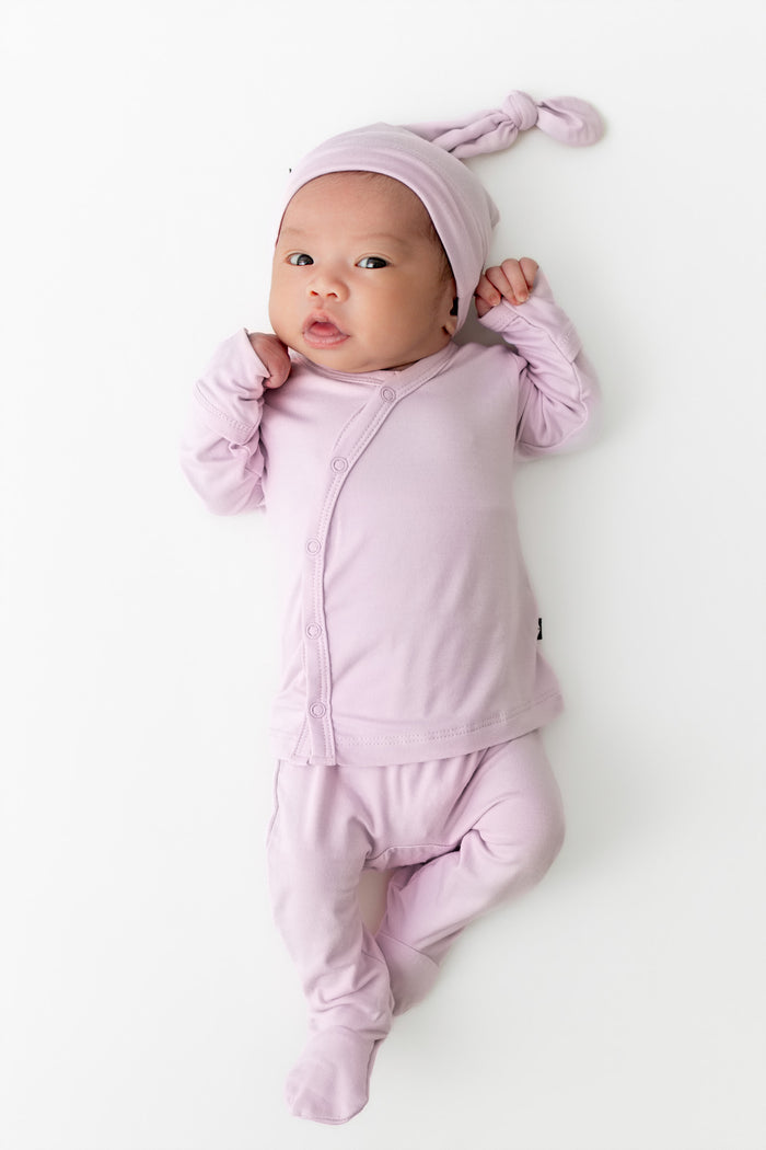 Baby in light purple outfit with matching hat on a white background