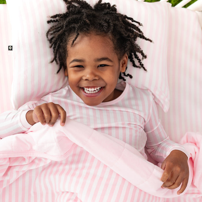 Young girl laying in bed on the small sakura stripe toddler pillow case and the Toddler Blanket in Small Sakura Stripe 1.0 on top of her
