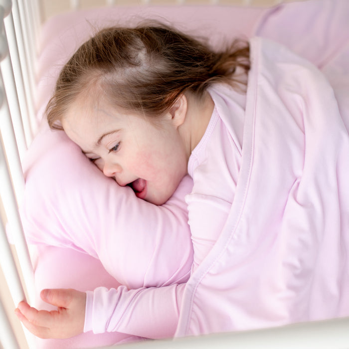 Young girl laying under the Toddler Blanket in Thistle 1.0 on top of a pillow with matching pillow case