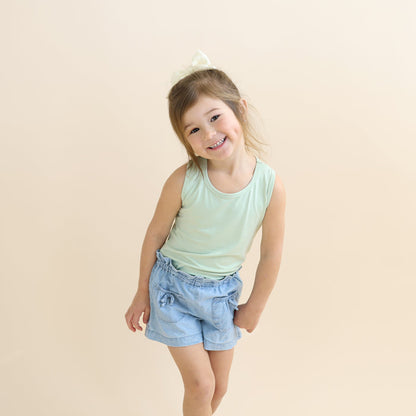 Young girl posing wearing the Toddler Tank Top in Basil with jean shorts