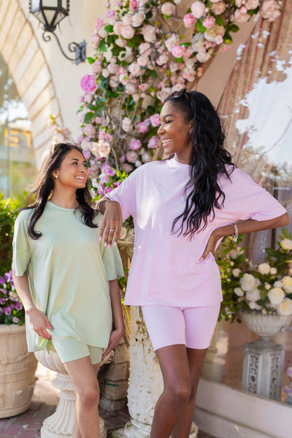 Two women standing outdoors with floral decorations in the background wearing biker short sets