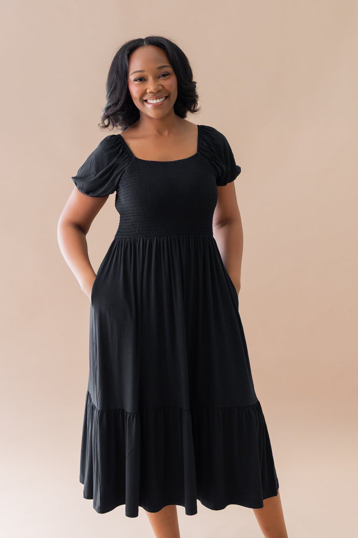 Smiling model wearing the Women’s Smocked Dress in Midnight with both hands in the dress pockets