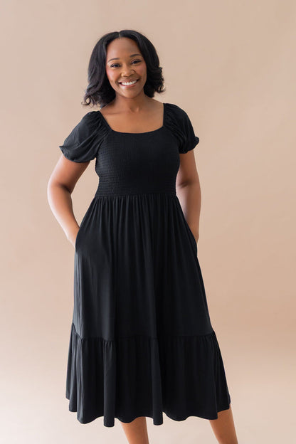 Smiling model wearing the Women’s Smocked Dress in Midnight with both hands in the dress pockets